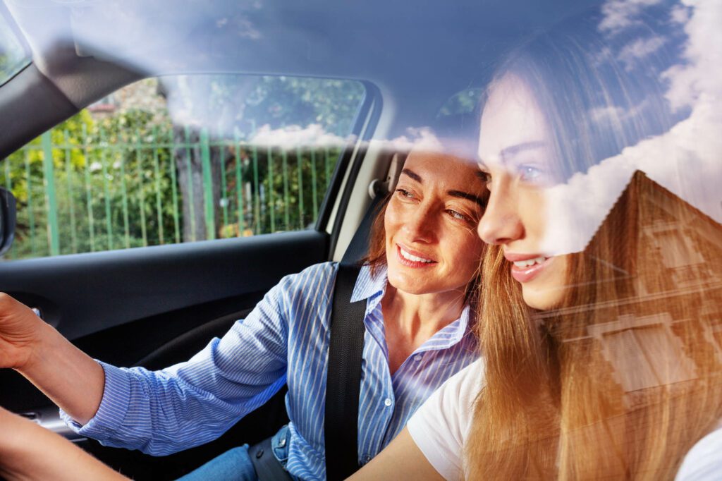 Portrait of beautiful young girl driving auto with her mother, viewed through car window